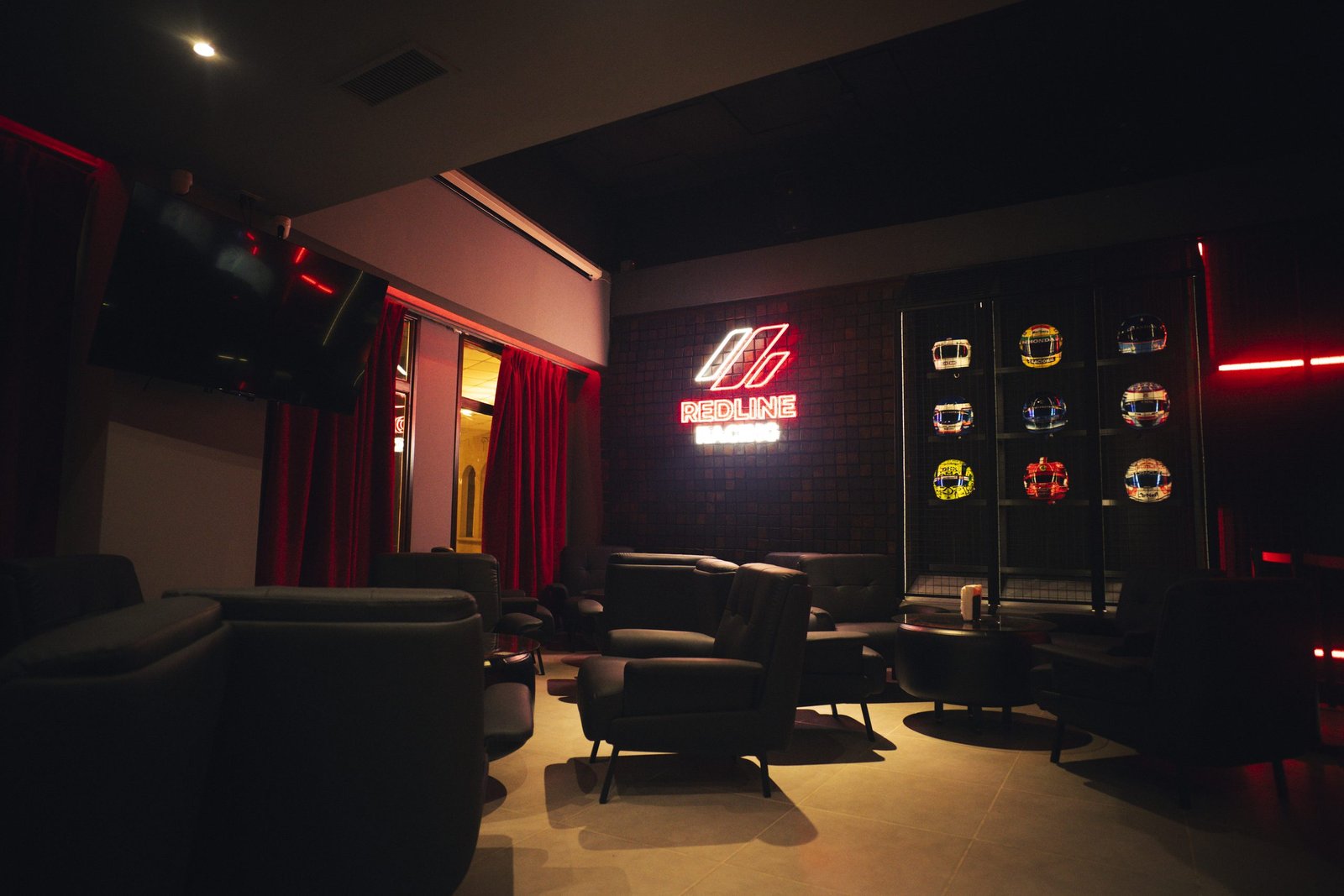 Lounge de Redline Racing con sillones, cartel de neón y vitrina de cascos